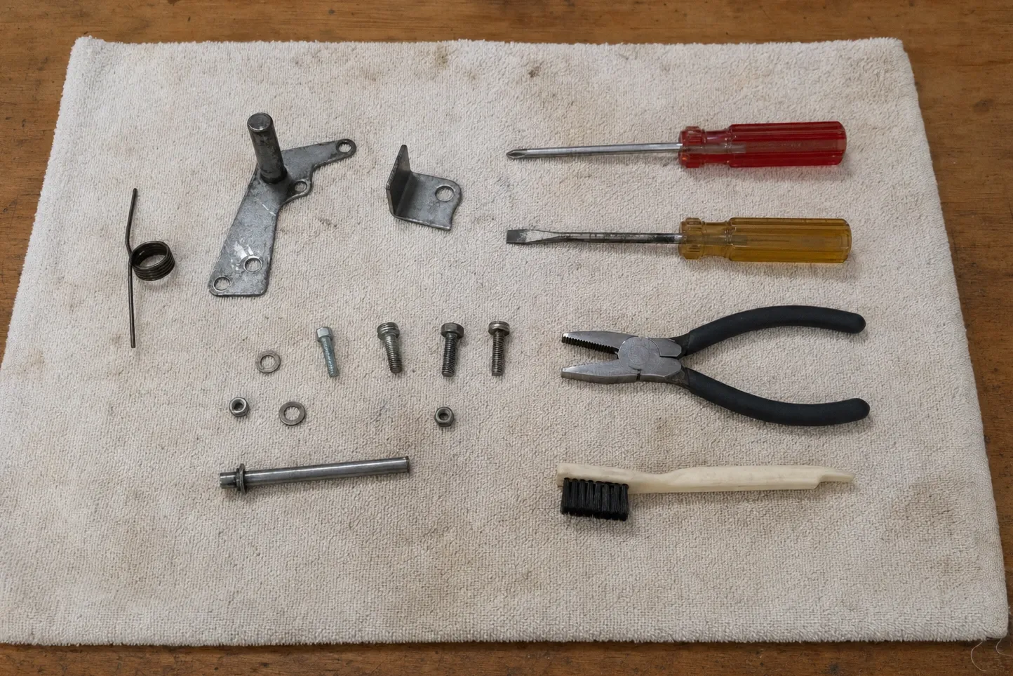 Door hinge arm with its pivot pin and torsion spring, an angle bracket, a pivot rod, bolts and washers set out on a cloth with drivers and pliers